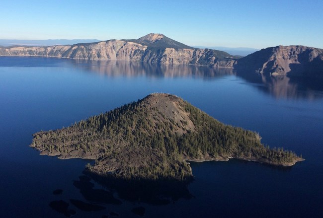 In Crater Lake is Wizard Island, a tree covered cinder cone volcano with a crater