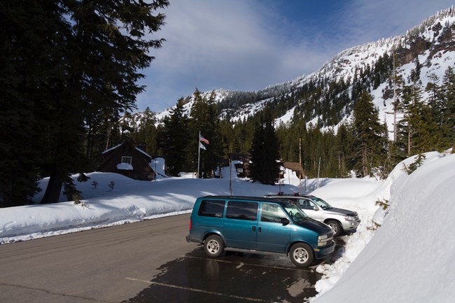 Two cars parked in a parking lot with high walls of snow around them