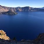 A view across the deep blue Crater Lake to a cone shaped Wizard Island to Lloa Rock