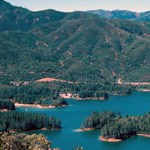 a blue-green lake with many small islands sits below a forest covered mountain range