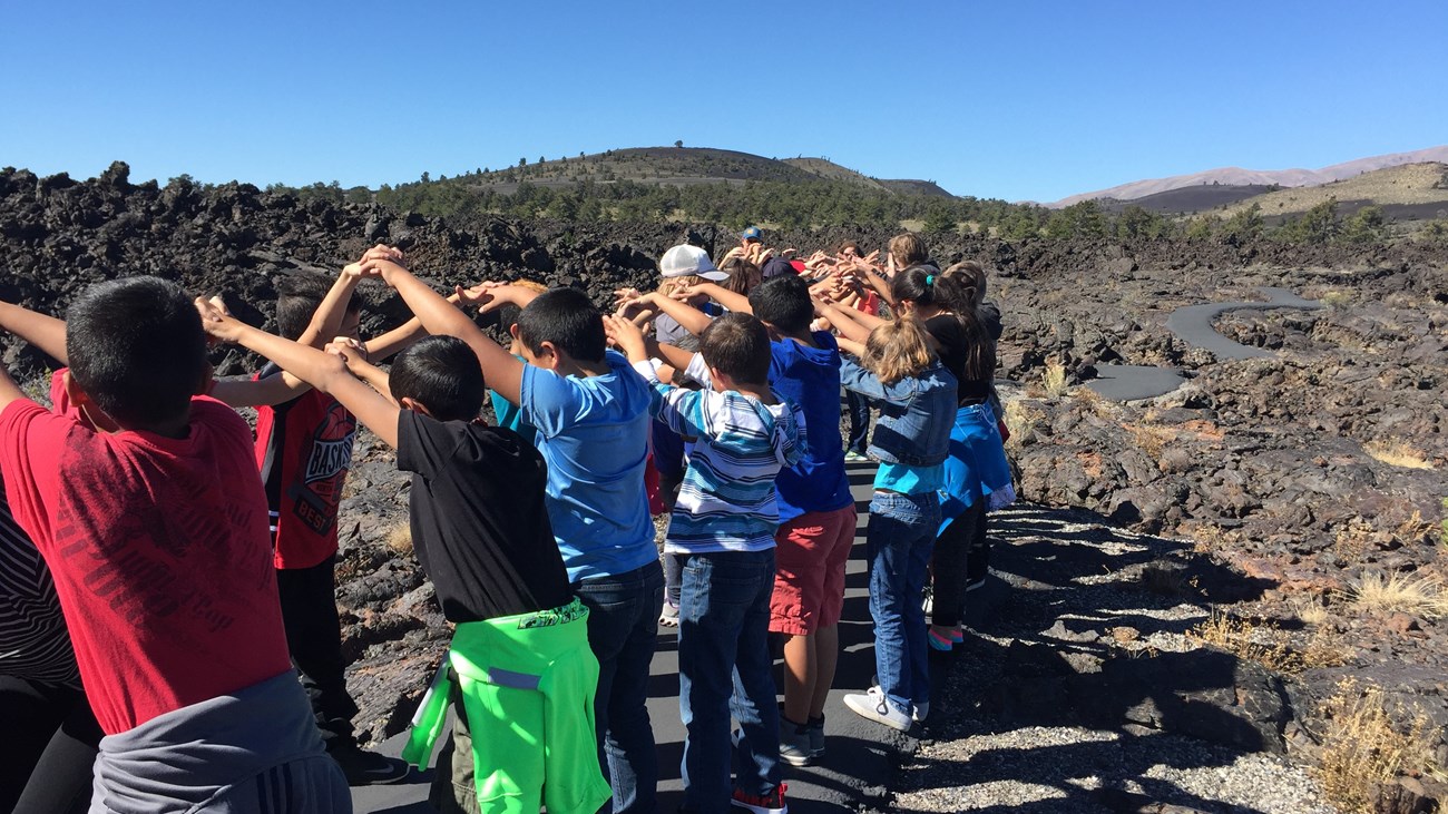 a line of students holding hands to create a tunnel on a trail