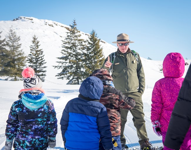 a ranger talking to a group of children with snowshoes