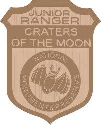 illustration of a wooden badge with an image of a bat wearing a ranger hat and the text "junior ranger, craters of the moon national monument and preserve"