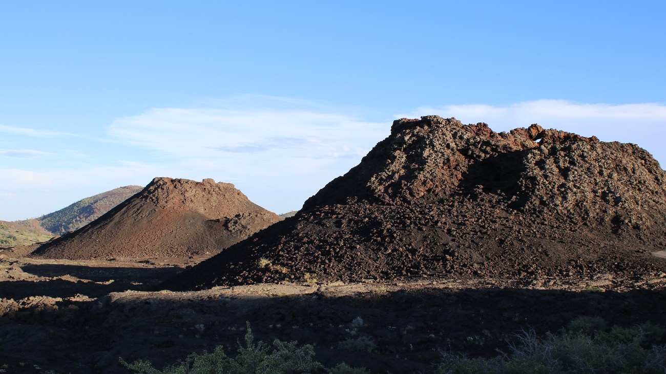 two small volcanoes with a cinder cone in the distance