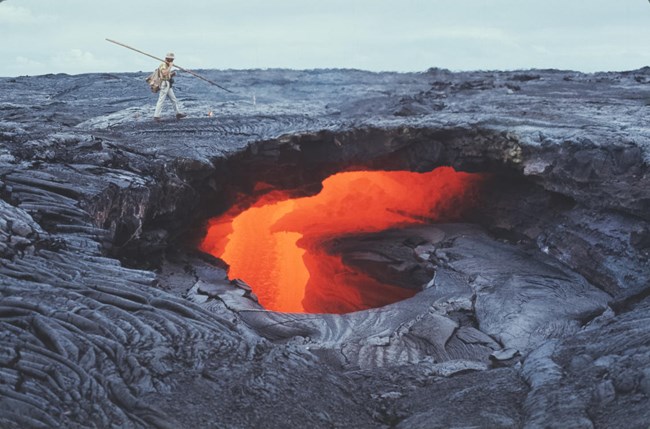 orange lava flows in a shallow cave as a man walks nearby
