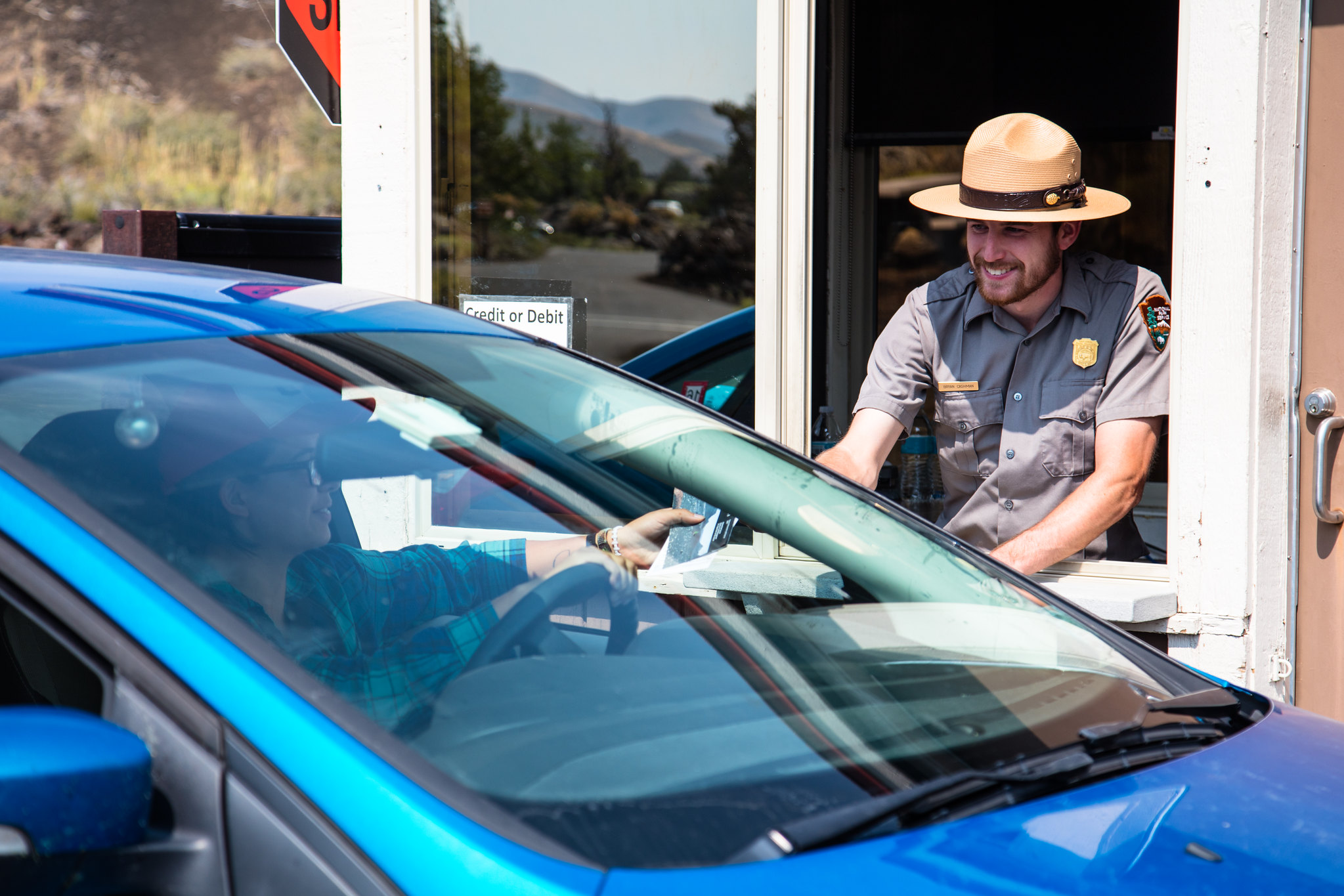 Entrance Station Ranger leans out of an entance station window and hands a pamphlet to a guest in a vehicle.