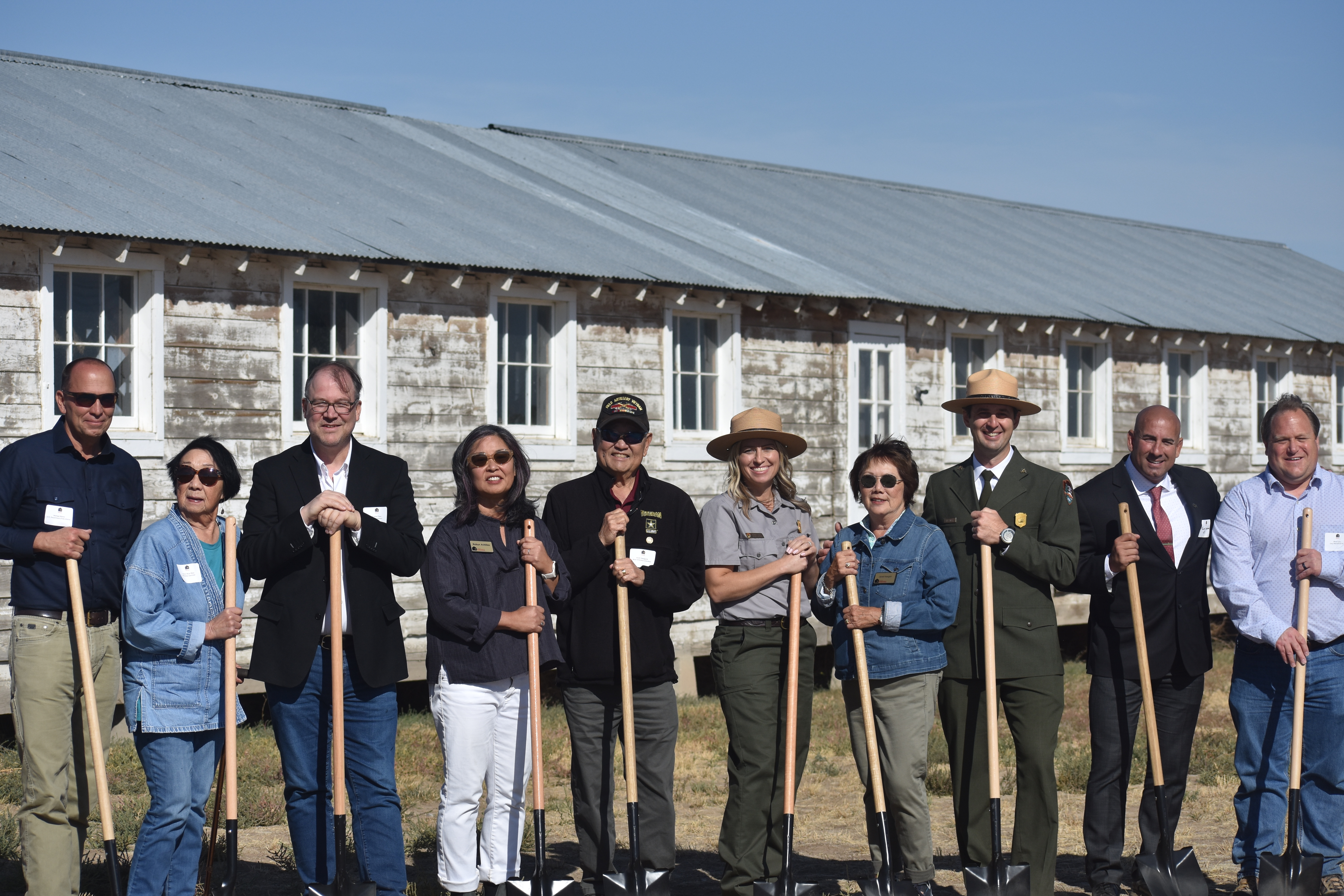 A group of ten people stand in a line facing forward while holding shovels.