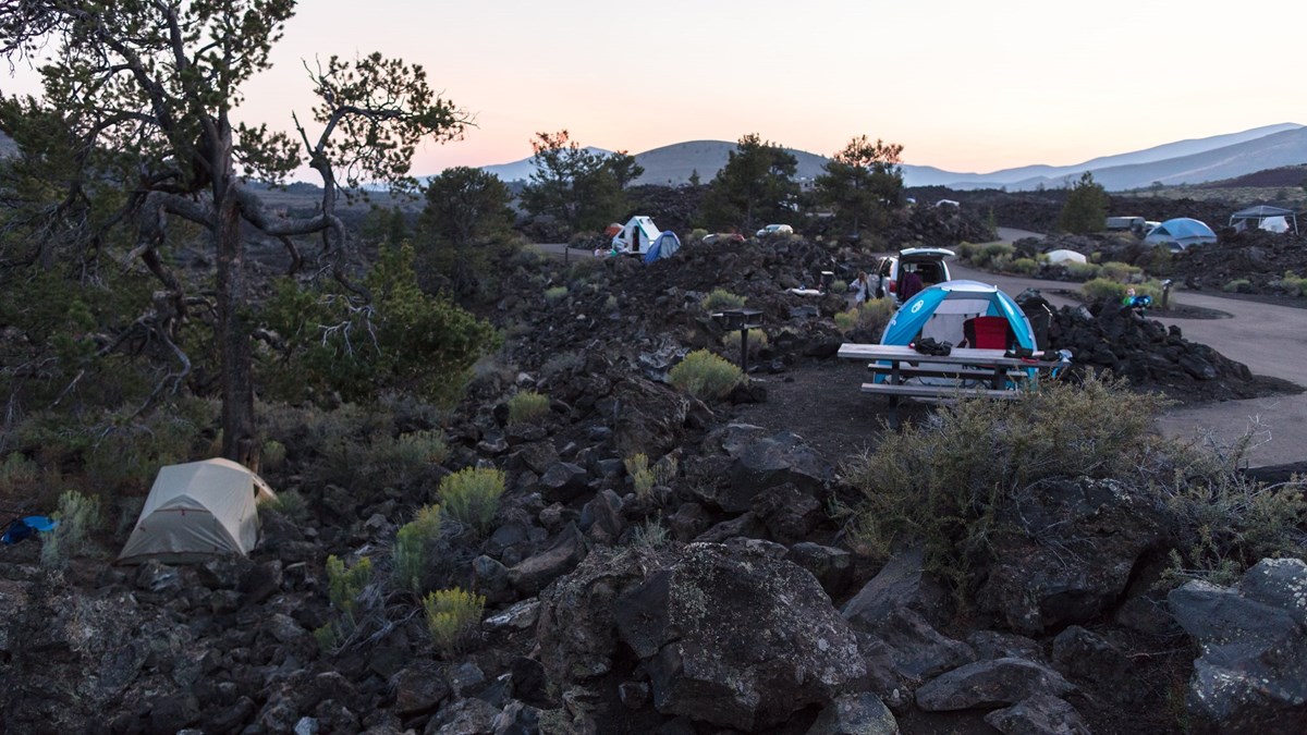 A tent and a picnic table within a rocky campground at dusk