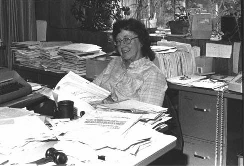 Hester Davis seated a desk with many reports.
