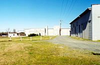 <three image series> Planting Design Compatible with the Historic Character. The existing site of this former textile mill is characterized by gravel driveways/lots, paved lots, and some grassy areas. This unadorned industrial site is consistent with the property's historic condition, as documented by old photographs. To complement the conversion of the property to a multiple-use project, a redesigned parking scheme will be introduced to the site. Grassy areas will continue to be significant site components. While trees will be planted on the site, they will be concentrated primarily at the perimeter of the parcel, with some limited placement near the buildings. Thus, the buildings and the site will not be overwhelmed by an incompatible planting scheme, and the character of the open, partially hard-surfaced industrial site will be preserved. Photos/Drawing: NPS files