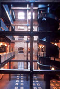<three photo series. This new atrium meets the Standards for Rehabilitation. The new atrium is very small in comparison to the building's size and covers less than 10% of the building footprint. Retaining the wood post and beam structure helps to show that the atrium is a new feature that has been created by cutting out a portion of the interior of the historic building (shown). The package chute was retained as a character-defining feature of the historic industrial building (shown). Photos: NPS files