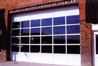 The existing garage door has been replaced with a new insulated overhead door with glass panels. It can be used, when needed, while the side door to the right of the overhead door serves as the street entrance and it did historicaly. It is important to emphasize that a functional garage door was not required in order to maintain the historic character of the building. A fixed partition made of wood or metal that resembled a traditional garage door would also have been appropriate.