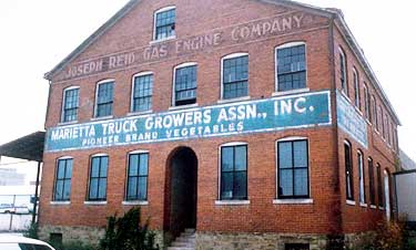 This 1880 manufacturing facility is located at the edge of a historic district. Constructed in red brick, it is a simply detailed, 2 story, gabled structure with a large one-story section in the rear. It displays characteristics typical of its function as an industrial building--large door openings, numerous windows, and a covered loading dock (the profile of which can be seen at the far left). Photos: NPS files.