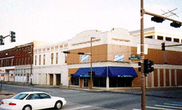 This two-story brick commercial building (see photo, below) was originally constructed ca. 1876. In 1916, the corner section was remodeled in the Craftsman style and given a new distinctive roof line. The red brick walls have been painted. Other distinctive storefront features, such as the second floor windows and transoms are obscured by incompatible coverings added in the 1960s. Photos: NPS files.
