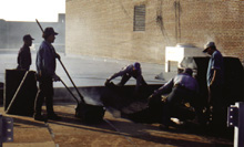[Photo] A photograph showing the application of the first ply of hot built-up roofing over perlite insulation board