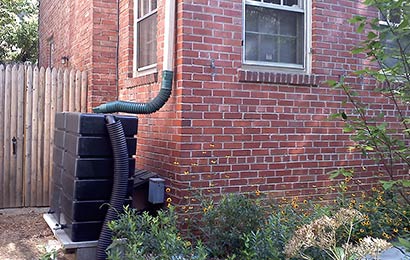 Rainwater collection tank connected to the downspout of a brick house.