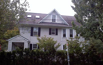 Two-story frame house with a central gable in the roof and two square skylights to the left of the gable.