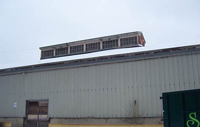 Exterior of an industrial building with metal siding, no windows and a monitor with windows on the roof.