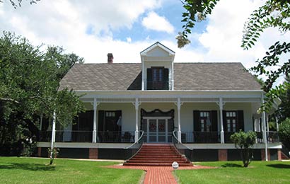 One-story white frame house with central dormer in roof, a wrap-around porch and shutters flanking the windows facing the porch.