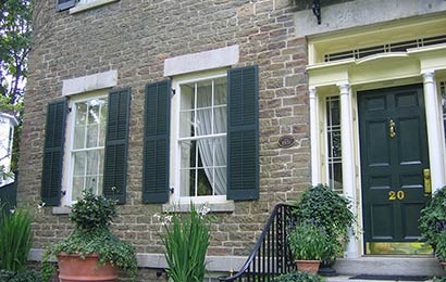 Detail of the exterior of a stone house with storm windows and shutters.