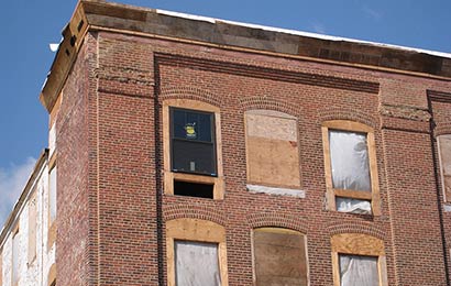 Red brick building with boarded-up windows and window openings that have been blocked down to accommodate smaller windows.