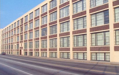 Mill building with multi-light metal windows, red brick spandrel panels, and masonry framing elements.