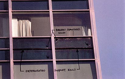 Detail of windows in a steel and glass curtain wall, with hand-written notes pointing out “Deteriorated support rails” and “Broken spandrel glass”; also with two different tints of glass.