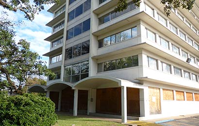 White masonry 1950s office building with projecting sunshades built-in between each floor and walkways with covered arches at ground level.