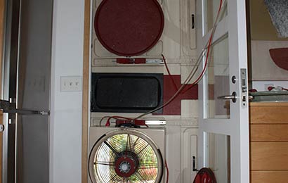 Interior of the same front door show with the fan in the lower part of the door and other mechanical equipment attached to the upper part of the door.