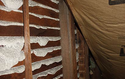 Dried foam insulation overlapping framing in an attic.