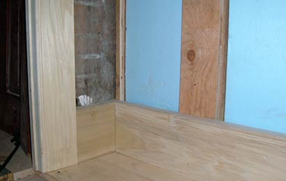 Rigid insulation installed between wall framing above a wood baseboard. 