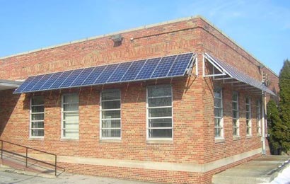 Rear of red-brick post office with solar panels used as awnings over the windows.