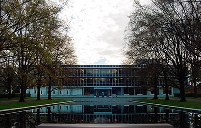 Trees flanking a pool of water in front of an International Style office building.