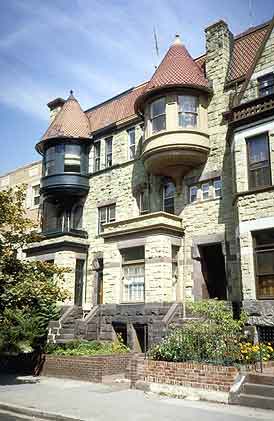 This is an image of 3-story urban row houses comprised of rough-cut stone, featuring half-round projecting bays with conical roofs and a series of complex window and door openings. The image rolls over to provide the correct answer. Screen Reader users see text-only link, left, for answer. Photo: NPS files.