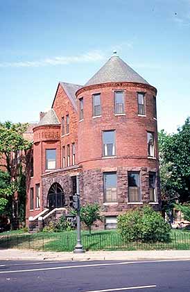 This is an image of a brick and stone urban rowhouse and yard located on the corner of two converging streets. The residence features a corner tower and arched doorway. The image rolls over to provide the correct answer. Screen Reader users see text-only link, left, for answer. Photo: NPS files.