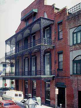 This is an image of 3/1/2 story building with a distinctive roofline profile and large window openings. The most important feature, however, it its lacy wrap-around porch.