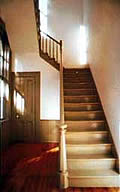 This is an image of a modest stair hall with a utilitarian stair, slender newel post and handrail, paneled dor, wood wainscoting, and simple trim. Photo: NPS files.