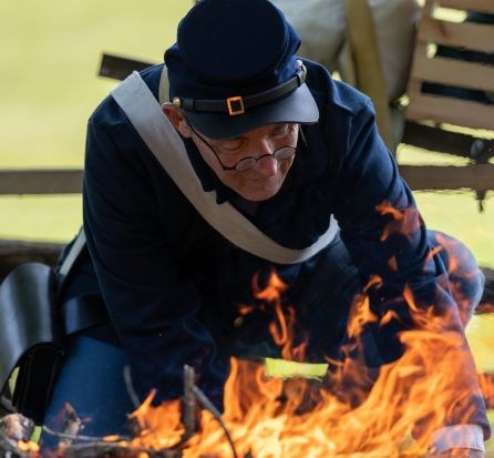 Male historical reenactor dressed in Union Soldier uniform kneeling in front of a campfire