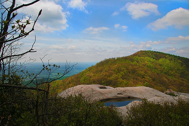 Aerial view of water-filled pothole and rounded mountain covered in fall foliage.