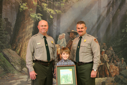 Park Ranger Butch Davis and Superintendent Mark Woods congratulate Junior Ranger Dakota Saylor