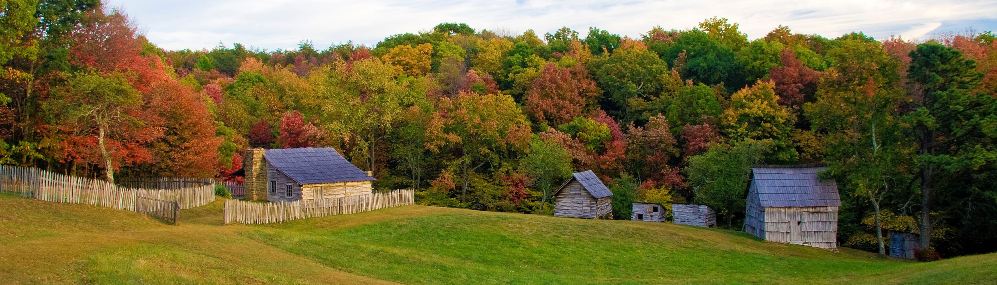 Hensley cabins in a field with the fall leaves in the background.