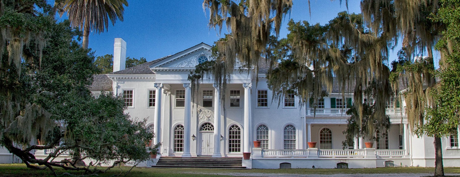 Large white mansion with live oak trees in the foreground