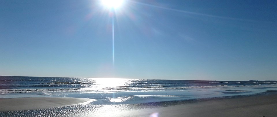 Blue water waves crashing on a white sandy beach under intense sun