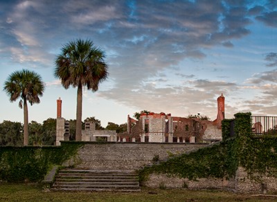 ruins of a large mansion; brick and stone work still standing, set upon a walled terrace with palm trees