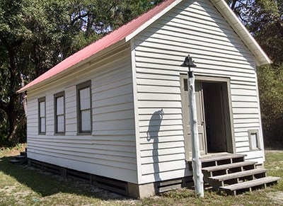 one room white church; church bell on pole it front; corner stone with founders' names