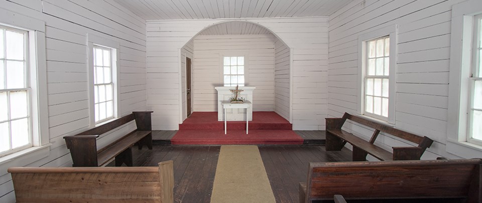 Single room church with white walls, wood floor, altar and pews