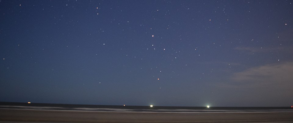 beach view at night under a starry sky with boat lights on the horizon