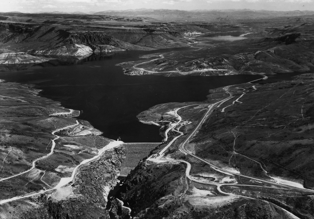 Historic black and white aerial image of a full reservoir. Roadways, mesas, and structures surround the water's edge.
