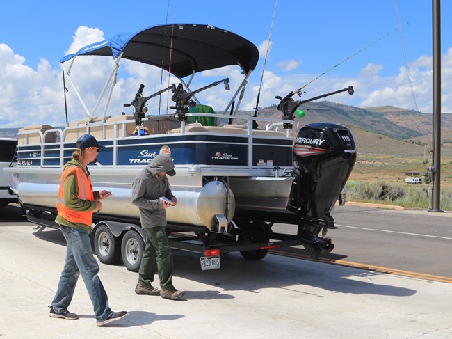 Two people wearing uniforms walk towards a trailered boat and vehicle.