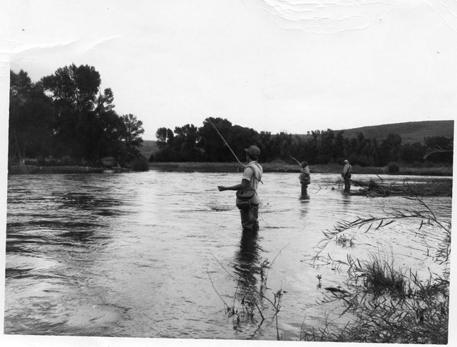 Black and white image of people fly fishing along a river